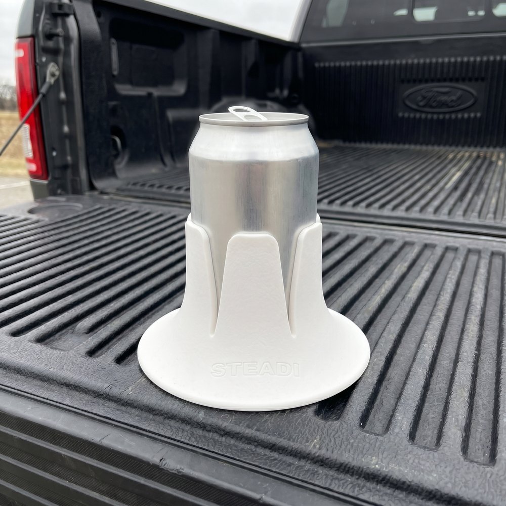 A can standing in a white Steadi base on the ribbed plastic bed liner of a pickup truck, tailgate down.